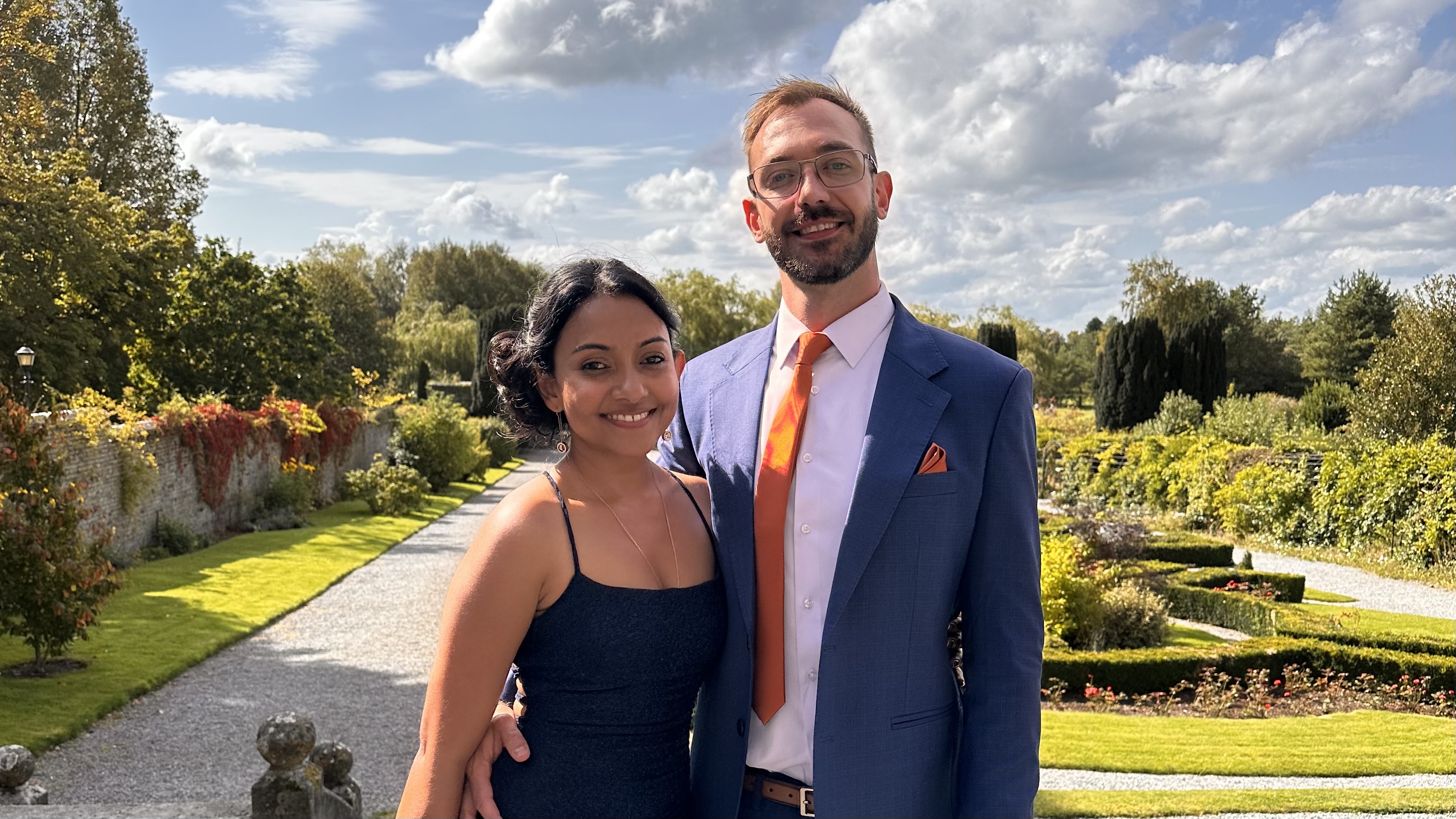 Kari and Anton posing together in a sunlit formal garden