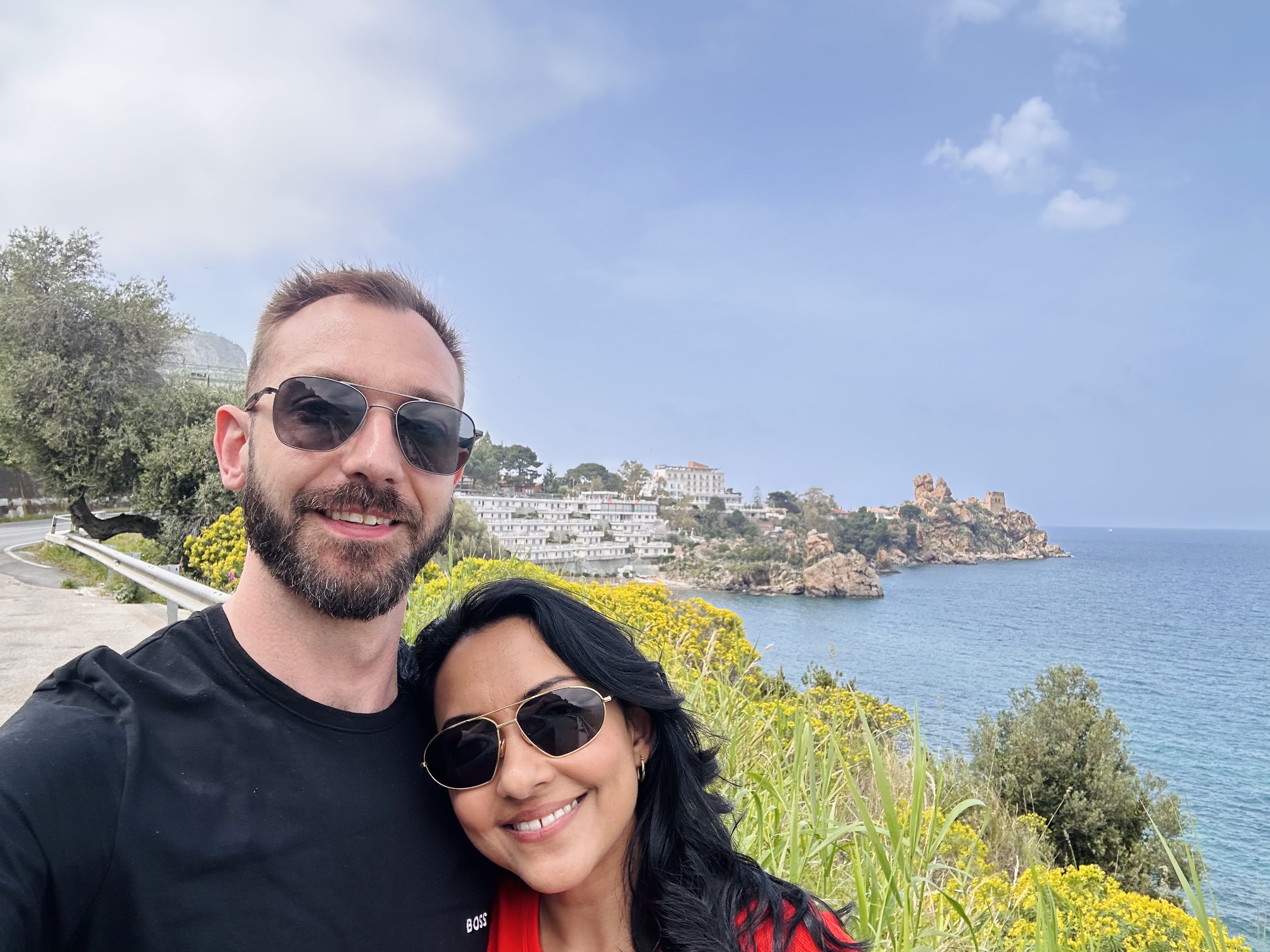 Kari and Anton smiling in sunglasses on a sunny coastal overlook
